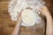 Female hands knead the dough on a wooden table, sprinkled with flour, close-up, selective focus, home cooking concept, copy space