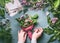 Female hands making flowers bouquet arrangement with green leaves decoration on working gray table with florist tools and accessor