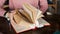 Female hands with neat manicure and a large clock leaf through a thick book with many bookmarks lying on the table.