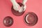 Female hands in pearly white gloves washing beautiful ceramic plates on trendy pink background. Household chores concept