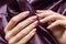 Female hands with pink nail design. Pink nail polish manicured hands. Woman hands hold purple fabric