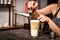 Female hands pour ingredients into a large transparent glass of latte coffee