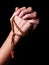 Female hands praying holding a beads rosary with a cross or Crucifix on black background