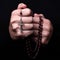 Female hands praying holding a rosary with Jesus Christ in the cross or Crucifix on black background.