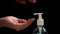 Female hands press the antiseptic dispenser, close-up, dark background