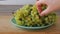 Female hands putting white grape clusters on a plate on a wooden table