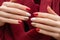 Female hands with red nail design. Gold and white nail polish manicure. Woman hands on red fabric background