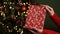 Female hands in red sweater hold Christmas New Year gift box on background of Christmas tree.Giving gifts for holidays.Christmas