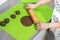 Female hands roll a dough with a wooden roller on a green silicone coffee table lying on the kitchen counter.