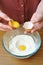 Female hands separate the egg white from the yolk over a bowl of wheat flour in the kitchen