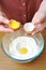 Female hands separate the egg white from the yolk over a bowl of wheat flour in the kitchen