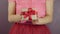 Female hands are showing present gift box with red ribbon bow, close up. Wrapped in craft paper gift with tied bow for St. Valenti