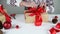 Female hands showing wrapped present in kraft paper box with red ribbon bow on a white wooden table at home.