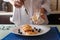 Female hands spkinkling honey on traditional syrniki or cottage cheese pankaces with blueberries and honey on white plate with blu