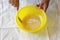 Female hands sugar with a raw egg in a yellow bowl, on a white towel background. Step by step cooking of pancakes. Step 3. Close-