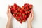 Female hands touch heart made tasty strawberry on white background, top view. Summer berry