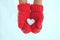 Female hands in warm red crocheted mittens with snowy heart. Whi