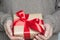 Female hands in woolen beige sweater holding beige box wrapped in craft paper with red ribbon. Close up.