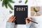 Female hands in woolen sweater write a wish list for New Year 2021 in black notepad