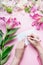 Female hands write with pencil greeting card on Blank envelop on pink table background with lily flowers and florist decoration eq