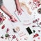 Female hands writes in notebook on white desktop with empty screen smartphone, cup of coffee, glasses, make up cosmetics, flowers