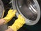 Female hands in yellow latex gloves for cleaning with a sponge wash the dirt around the drum of a black washing machine