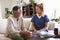 Female healthcare worker sitting with a senior Hispanic man in his living room during a home visit