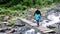 Female hiker crosses a wild mountain stream on a wooden bridge in a forest landscape