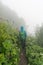 Female hiker on a narrow hiking path in an alpine meadow with high grass and wildflowers in thick fog