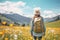 Female hiker standing in flowering alpine meadow and admiring a scenic view from a mountain top. Adventurous young girl with a