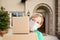 Female Holding Delivery or Moving Boxes At Front Door of House Wearing Medical Face Mask