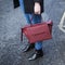 Female holding a maroon leather handbag wearing denim and black boots on a road