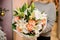 Female holds a bouquet lilies, orchids, pion-shaped roses in white wrapping paper