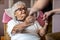 Female home carer supporting old woman to stand up from the armchair