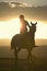 Female horseback rider and horse ride to overlook at Lewa Wildlife Conservancy in North Kenya, Africa at sunset