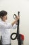 Female housekeeper holding vacuum cleaner pipe against gray background