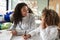 Female infant school teacher working one on one with a young schoolgirl, sitting at a table smiling at each other, front view, clo