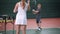 Female instructor teaching little boy playing tennis. Woman in white sport outfit standing in the court throwing yellow