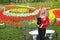 Female journalist standing with a microphone on a bright tulips lawn background