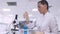 A female lab technician transfers a blue fluid sample to different tubes using a micropipette while sitting at a table