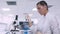 A female lab technician transfers a blue fluid sample to different tubes using a micropipette while sitting at a table