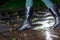 Female legs in black leather high boots on cobble the edge of rain puddle, closeup. Concept protection against rainy