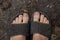 Female legs in black rubber flip flops stand on the ground top to bottom view