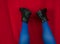 Female legs in blue tights black boots upside down on red background. Fashion modern style. Vivid contrasting colors