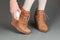 Female legs in brown suede boots on a gray background. Woman cleaning her suede shoes