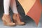 Female legs in brown suede boots under an umbrella on a gray background. Waterproof treatment for suede boots concept