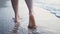 Female legs and feet walking along sea water waves on sandy beach. wounded legs woman walks at seaside surf. Splashes of water