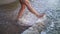 Female legs and feet walking along sea water waves on sandy beach. wounded legs woman walks at seaside surf. Splashes of water