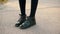 Female legs in patent leather shoes standing on asphalt road. Close up teenager girl feet in black patent leather boots