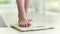Female legs stepping on white scale at home. Bare feet on a weight scale.